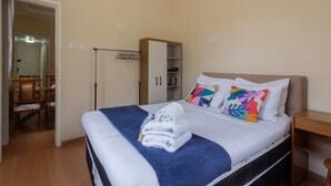 A neatly made bed with a blue blanket and white pillows, a wooden wardrobe, and a chair in a room with beige walls. - 8 Minutes From Copacabana Beach Br1010 (Rio de Janeiro)