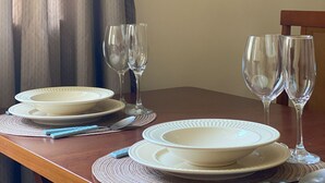 A dining table set with plates, bowls, and wine glasses, with a wooden chair and a curtain in the background. - 8 Minutes From Copacabana Beach Br1010 (Rio de Janeiro)