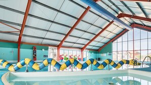 An indoor swimming pool with clear water, a tiled floor, and a ceiling with metal beams and windows.