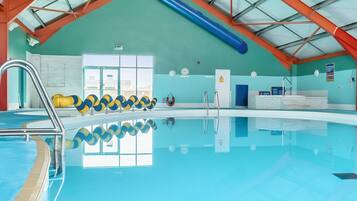 Piscina interna com teto alto, paredes de vidro transparente e painel de bolas azul e amarelo.