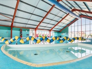 Piscina interior com teto transparente, borda azul e marcações de pistas coloridas.