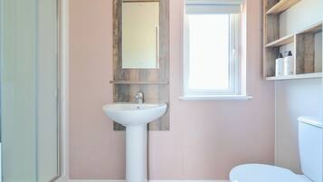 Un baño con un lavamanos blanco, un espejo, una ventana y un inodoro.