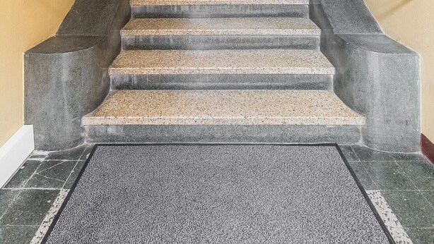Una escalera de granito con barandillas de metal que conduce a un rellano del segundo piso.