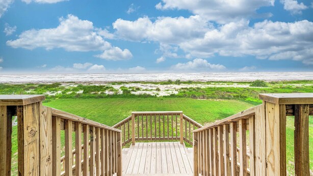 Een houten terras met uitzicht op een strand en een gazon.