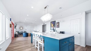Een moderne keuken met een groot eiland, witte barkrukken en een blauwe accentmuur.