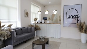 A modern hotel reception area with a grey sofa, a coffee table, and a reception desk. - UNO Hotel Jalal-Abad (Jalal-Abad)