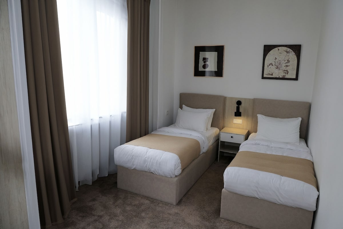 A hotel room with two beds, a nightstand, and a window with curtains.