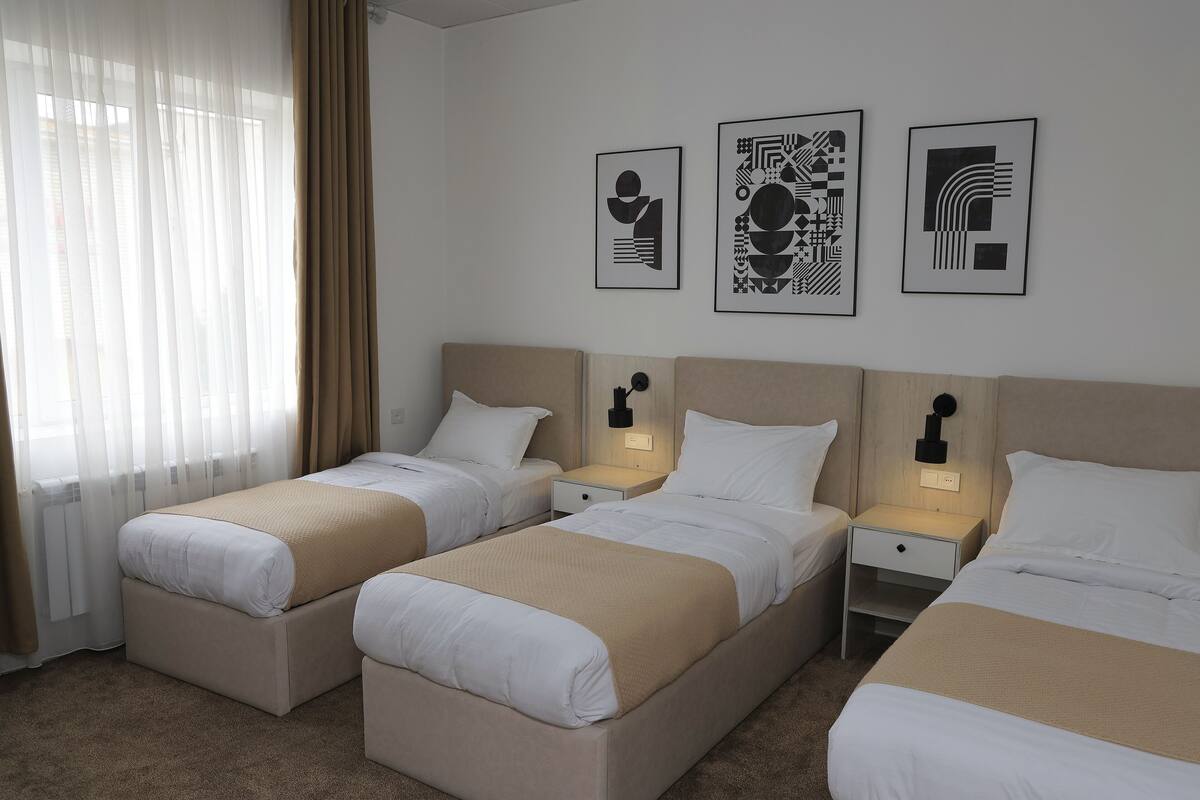 A hotel room with two beds, a nightstand, and three framed artworks on the wall.
