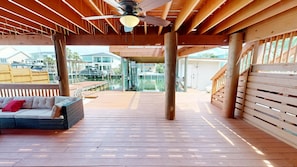 Um deck de madeira com ventilador de teto, um sofá com almofadas, e vista para uma marina com barcos.