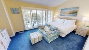 A bedroom with a bed, a sofa, a nightstand, and a window with blinds.