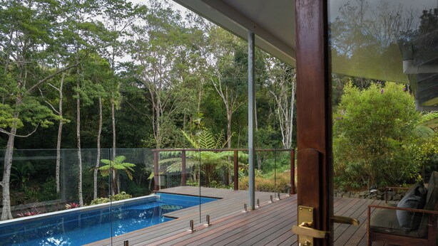 A wooden deck with a pool, surrounded by lush greenery and trees.