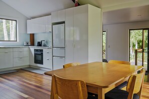 A modern kitchen with white cabinets, a built-in oven, and a dining area with a wooden table and chairs.