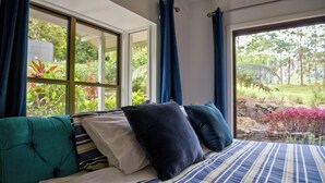 A bedroom with a large window, a bed with striped bedding, and a view of a garden.