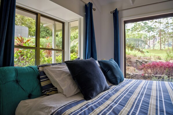 A bedroom with a large window, a bed with striped bedding, and a view of a garden.