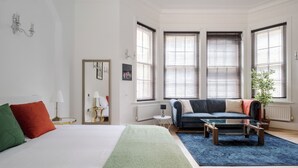 Una camera moderna con un letto, un divano, un tavolino da caffè e ampie finestre con tende.