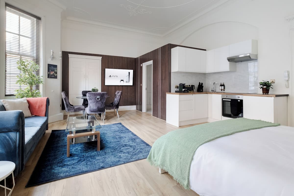 Ein modernes Hotelzimmer mit einem Bett, einer Sitzecke mit Glastisch, einer Küchenzeile und einem Fernseher.