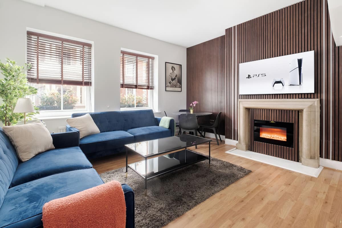 Ein modernes Wohnzimmer mit einem blauen Sofa, einem Glastisch und einem Kamin.