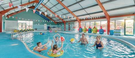 An indoor swimming pool with a covered roof, clear water, and colorful decorations.