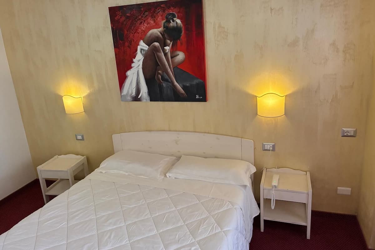 Ein Hotelzimmer mit einem Queensize-Bett, zwei Nachttischen und einem Bild an der Wand.