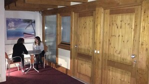 Habitación con paredes de madera y alfombra roja, que presenta un cuadro de un barco en la playa, una mesa y dos sillas.