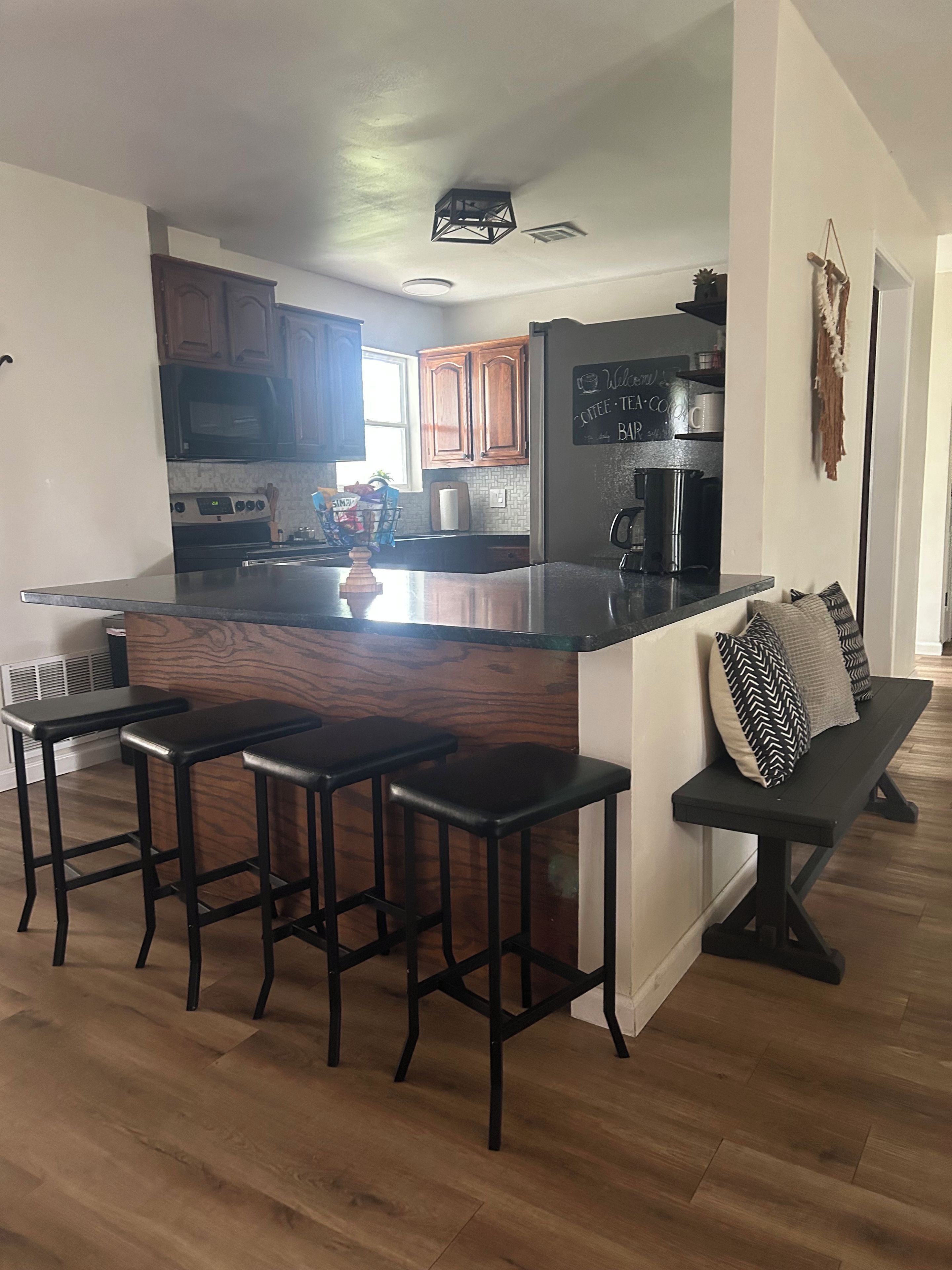 Una cocina moderna con una isla central, taburetes de bar, un banco, armarios de madera y un refrigerador.