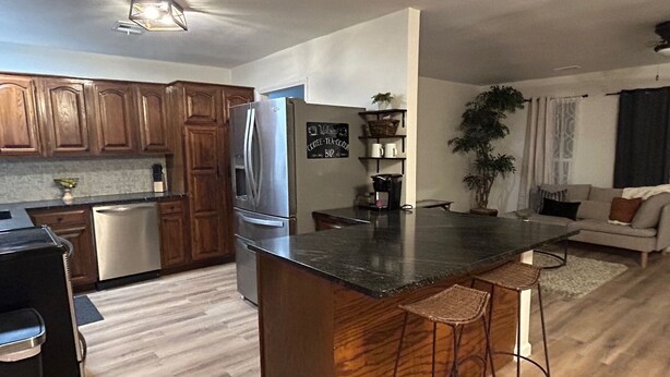 A modern kitchen with wooden cabinets, a stainless steel refrigerator, and a bar area with stools. - 3-bedroom house in peaceful Independence. Enjoy your stay (Independence)