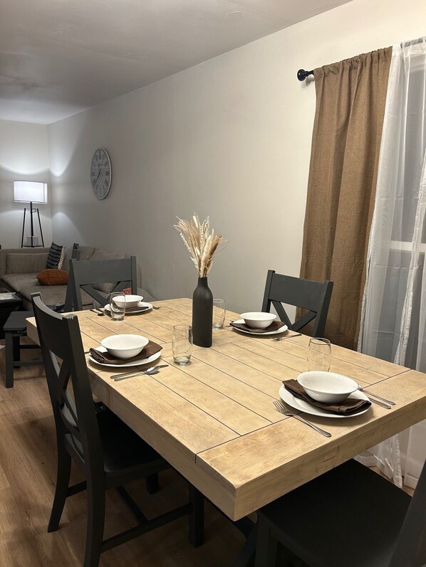 A dining area with a wooden table set for four, surrounded by dark chairs. A vase with dried flowers is placed in the center. - 3-bedroom house in peaceful Independence. Enjoy your stay (Independence)