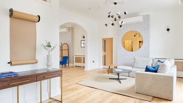 A spacious living room with a wooden floor, a round mirror, a sofa, and a coffee table. - Camden Road Hotel     (London)