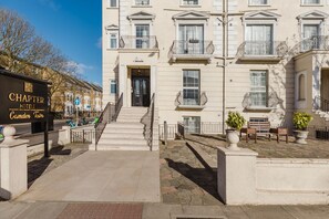 L’entrée d’un hôtel, avec un panneau indicateur, des marches et une zone pavée agrémentée de jardinières et de bancs.