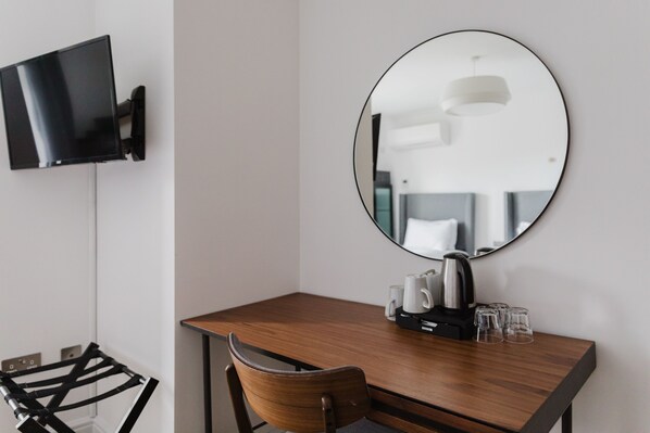 A modern hotel room with a wooden desk, a mounted TV, a round mirror, and a coffee maker. - Camden Road Hotel     (London)