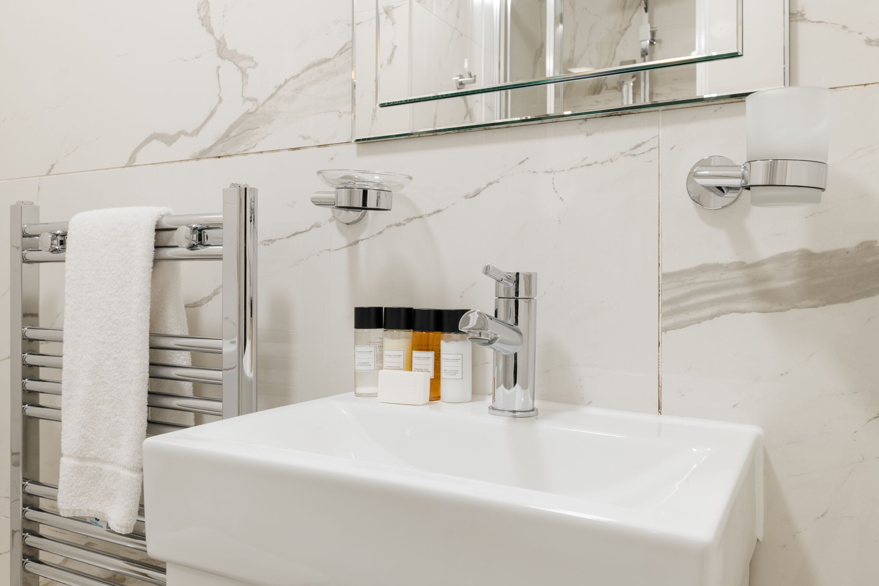 A bathroom with a white sink, chrome fixtures, a glass shower enclosure, and a towel rack with a white towel.