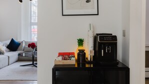 A modern living room with a sofa, a coffee machine, a framed abstract artwork, and a window. - Camden Road Hotel     (London)