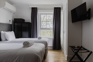 Une chambre d’hôtel avec deux lits, un téléviseur, un radiateur et une fenêtre avec des rideaux.