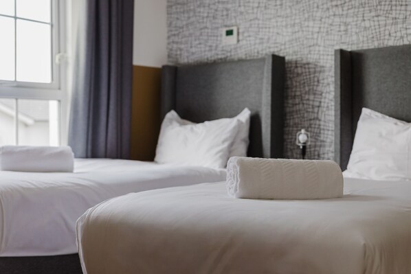 A hotel room with two beds, a window with curtains, and a textured wall. - Camden Road Hotel     (London)