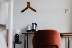 A room with a wooden hanger, a table with a kettle, a cup, and a glass, and a red chair. - Camden Road Hotel     (London)