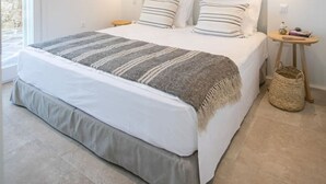 Une chambre dotée d’un grand lit, de deux tables de chevet, d’un luminaire fixé au mur et offrant une vue sur l’extérieur.