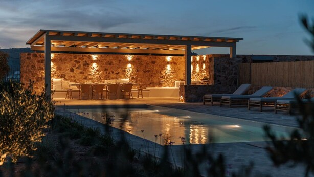 Un espace cuisine extérieur abrité, doté de murs en pierre, d’une piscine et de chaises longues.