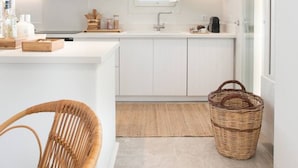 Une cuisine moderne avec des meubles blancs, un îlot central, des luminaires suspendus et une vue sur le ciel par une fenêtre.