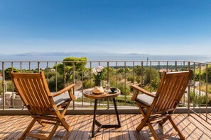 A balcony with two wooden chairs and a small table, overlooking a scenic view of mountains and a body of water.