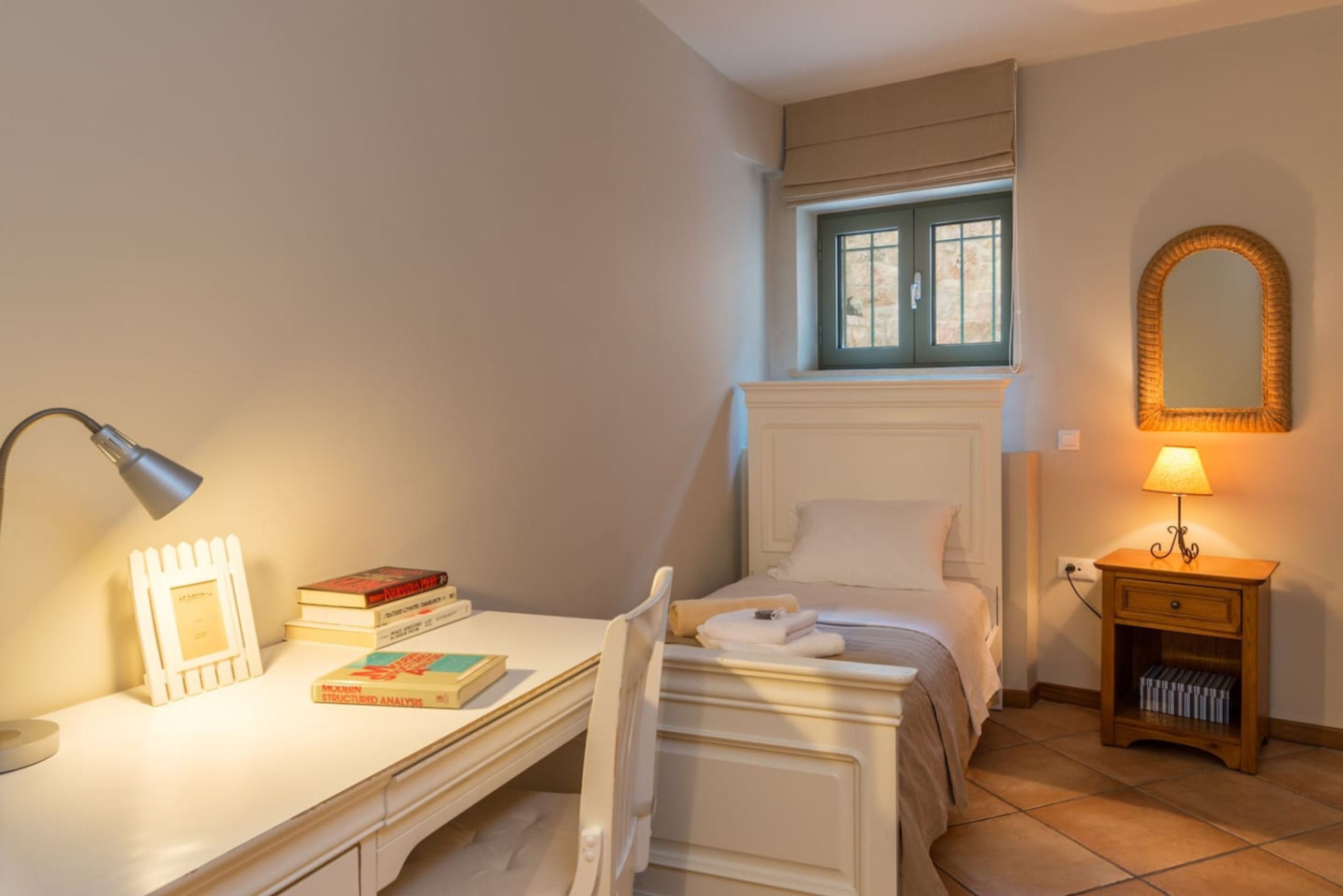 Une chambre à coucher comprenant un lit, un bureau, une chaise, une table de chevet avec une lampe, un miroir et une fenêtre.
