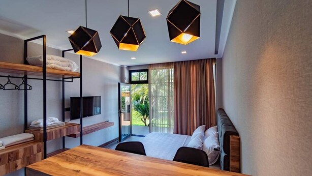 A modern hotel room with a wooden desk, a bunk bed, a flat-screen TV, and a large window with curtains. - Dachis Villa (Batumi)