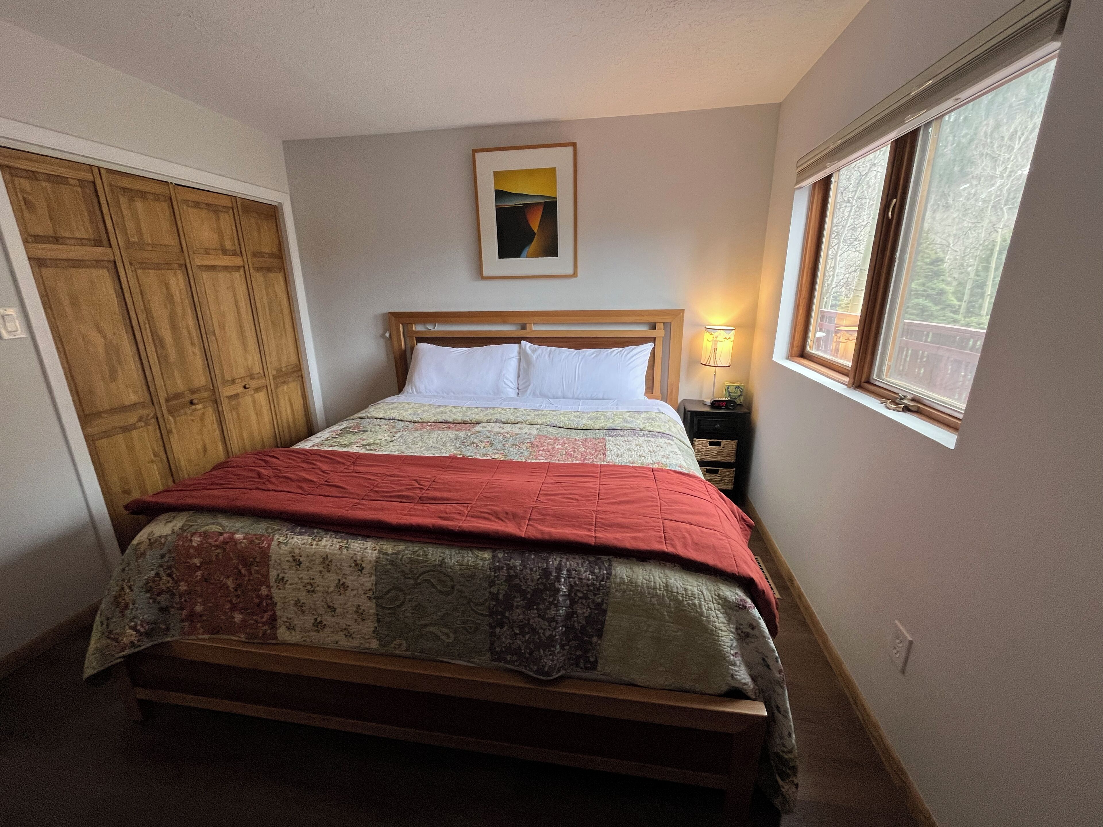 A bedroom with a bed, wooden wardrobe, a nightstand, a lamp, and a window.
