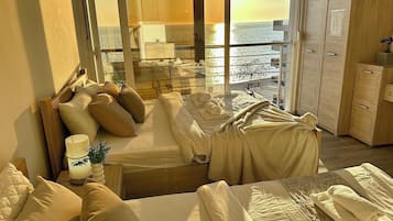 A hotel room with a bed, a seating area with cushions, a view of the sea, and a wardrobe.