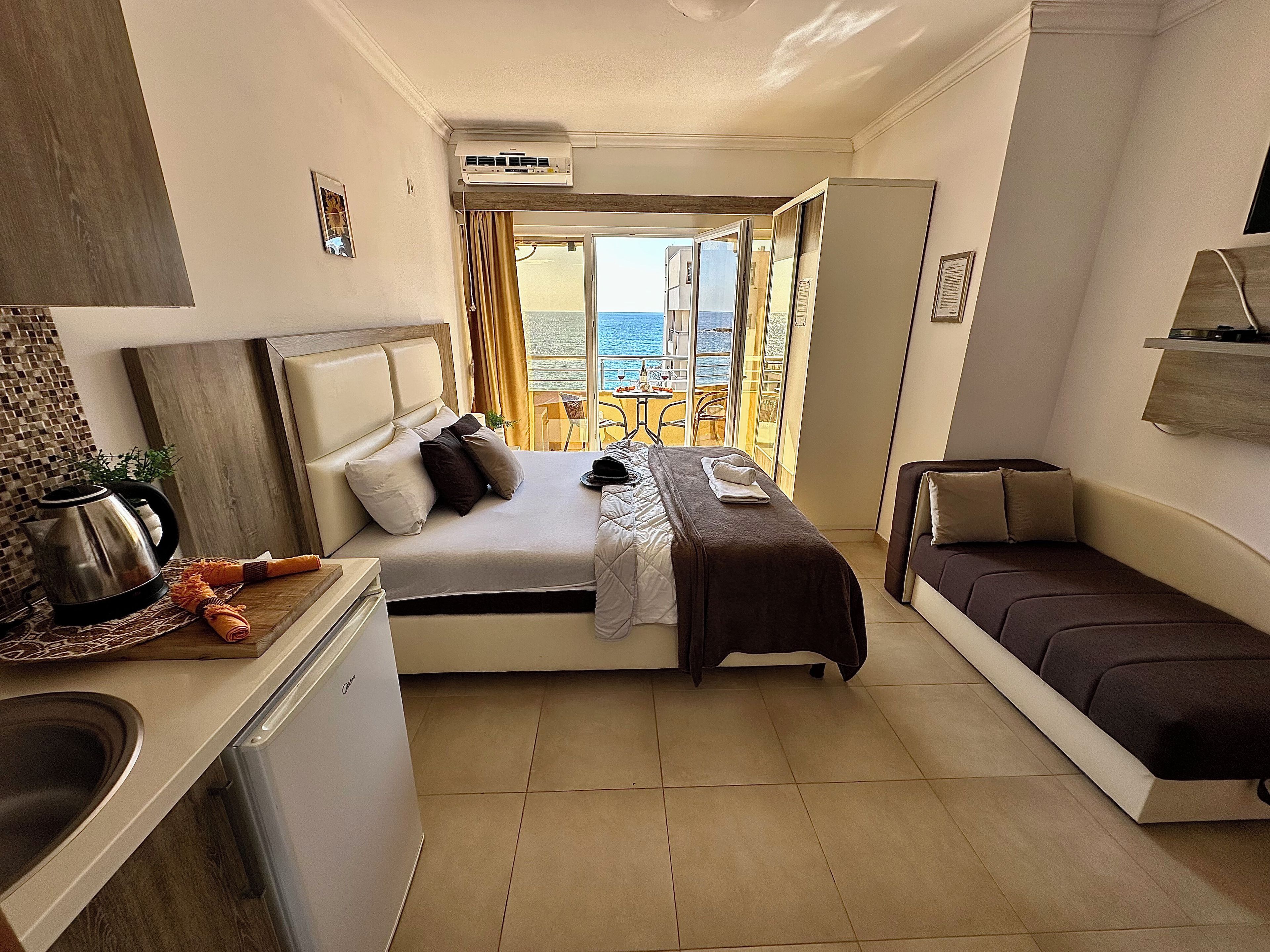 Habitación de hotel con cama, sofá, kitchenette y vistas al mar.