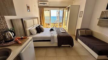 Habitación de hotel con cama, sofá, kitchenette y vistas al mar.