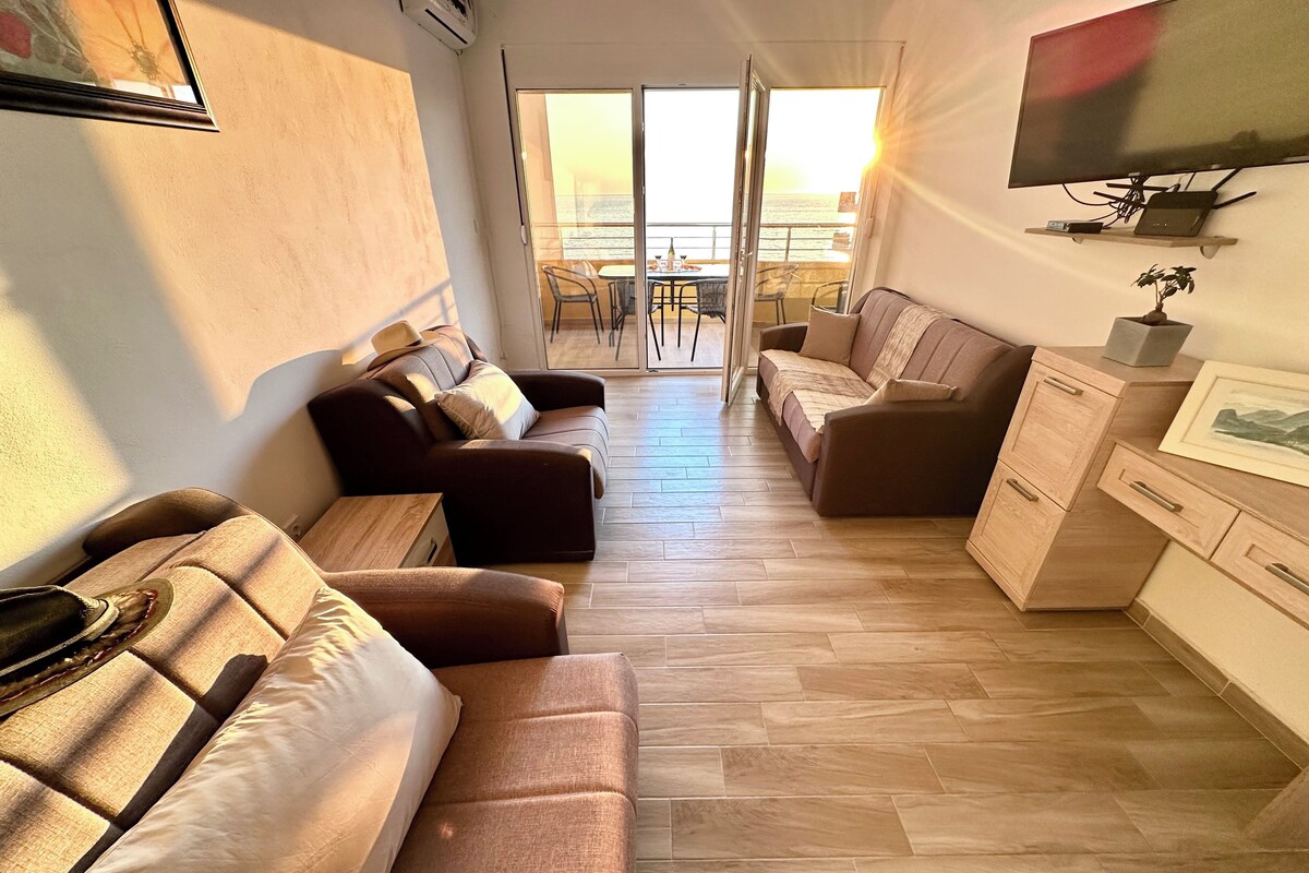 A modern living room with a sofa, a coffee table, a TV, and a balcony with a view.
