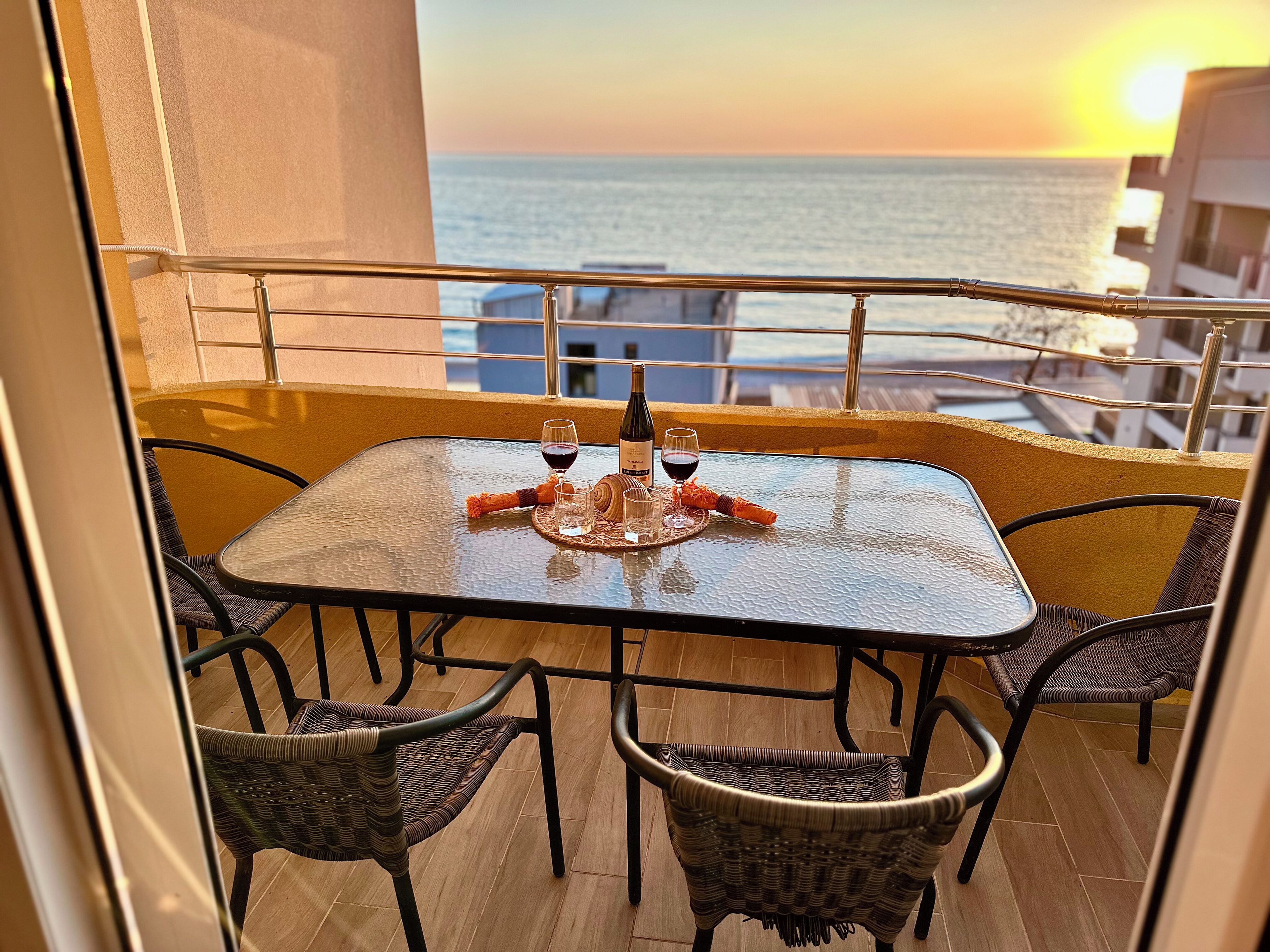 Un balcon avec une table dressée pour deux personnes, une bouteille de vin rouge et un verre de vin.