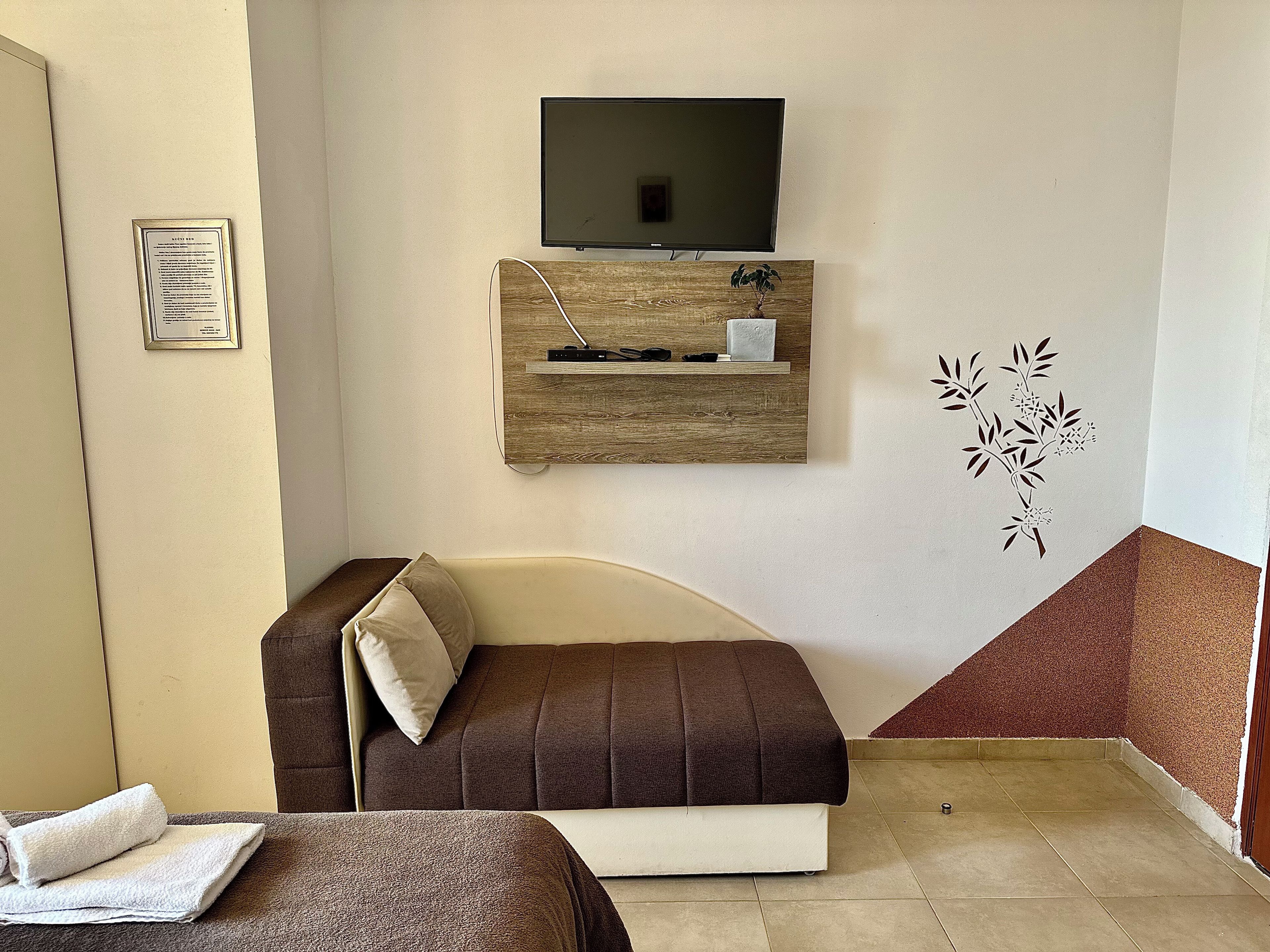 A room with a sofa, a television mounted on the wall, a small shelf with items, and a decorative wall piece.