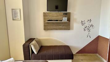 A room with a sofa, a television mounted on the wall, a small shelf with items, and a decorative wall piece.