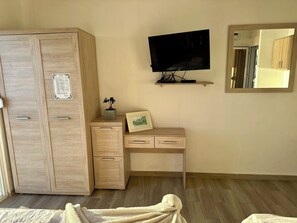 A bedroom with a wooden wardrobe, a desk with drawers, a mounted TV, a framed picture, and a potted plant. - Saray Hotel (Bar)